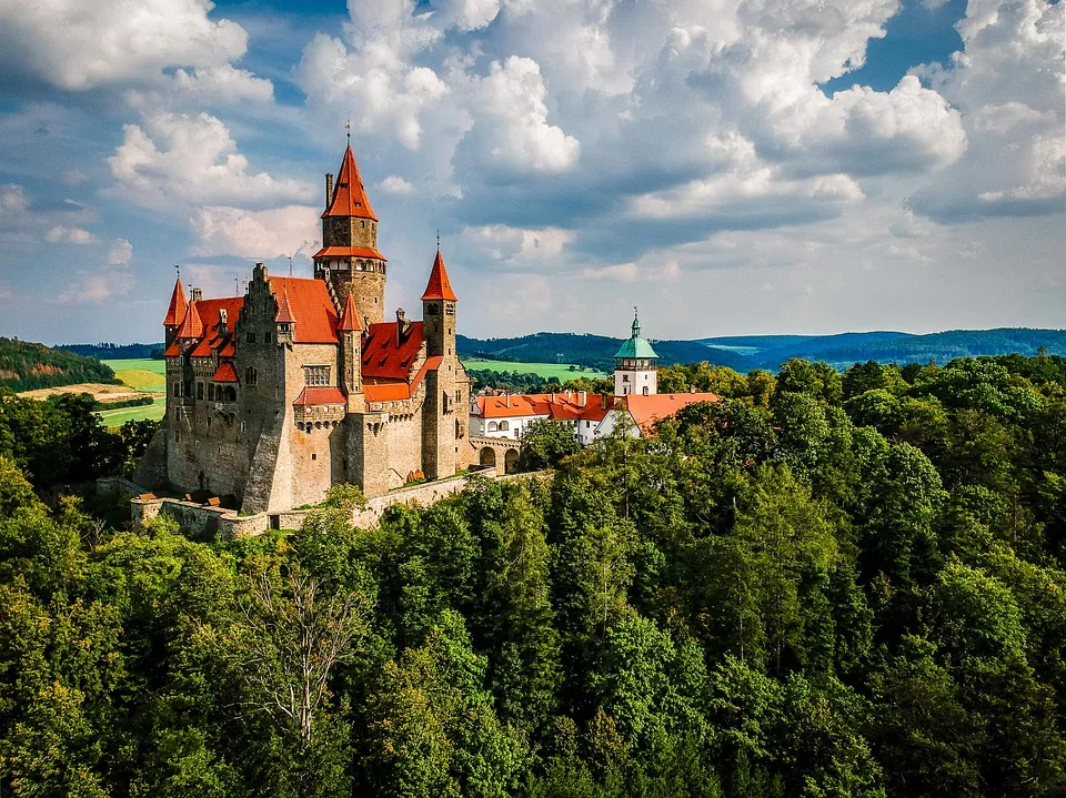 Hrad Bouzov s věžemi a červenými střechami nad zelení.