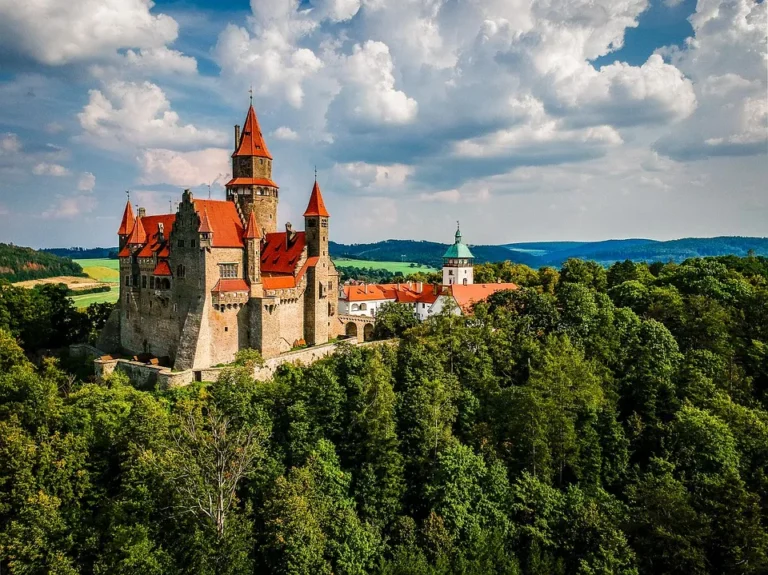 Hradní věže a červené střechy nad zalesněnou krajinou; ilustrační snímek.