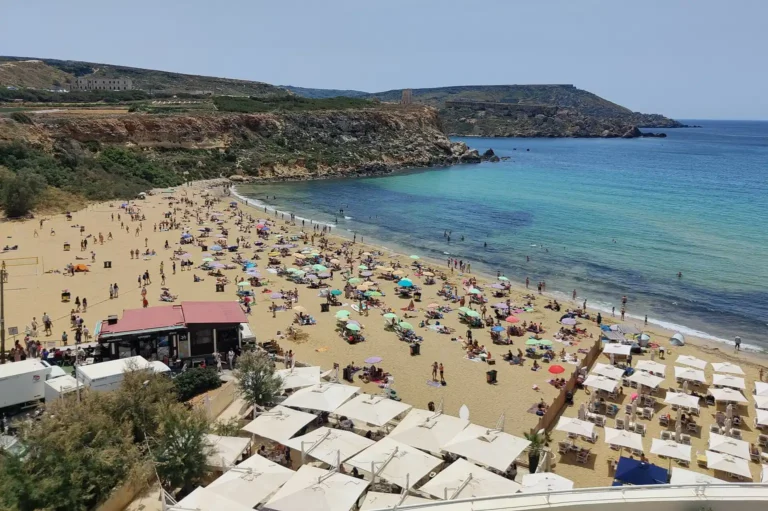 Písečná pláž Golden Bay na Maltě s návštěvníky a zátokou