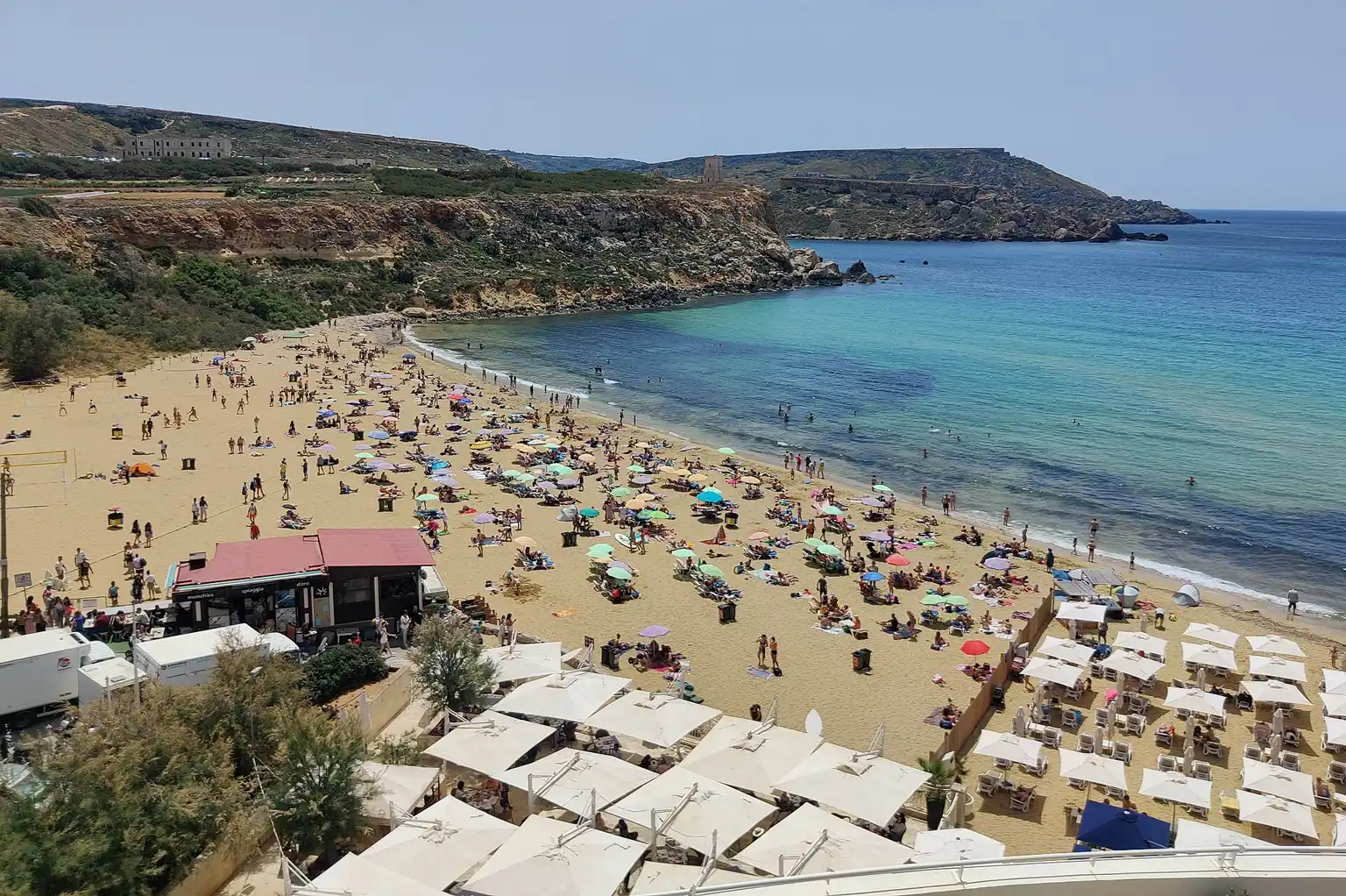 Písečná pláž Golden Bay na Maltě s návštěvníky a zátokou