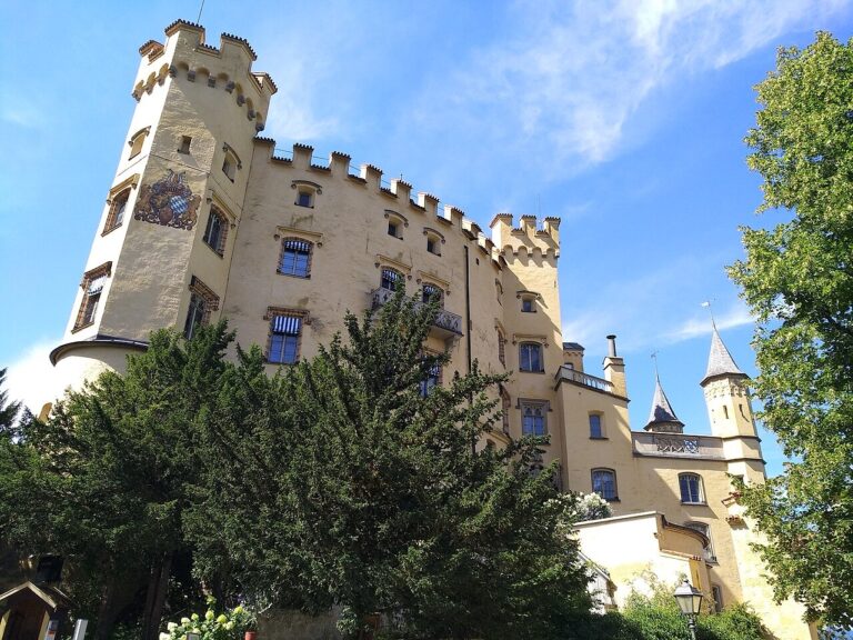 Žluté průčelí a věže zámku Hohenschwangau nad obcí