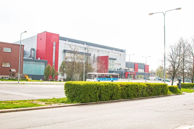 Budova Aquacentra Pardubice s šedou a červenou fasádou, pohled přes ulici a parkoviště