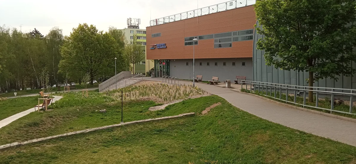Budova Aquaparku Kohoutovice v Brně s dřevěným obkladem a parkovou úpravou před vstupem