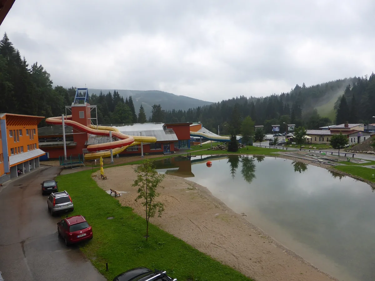 Budova aquaparku ve Špindlerově Mlýně s venkovními rourami tobogánů a jezírkem v popředí, snímek ze srpna 2014, tedy před renovací