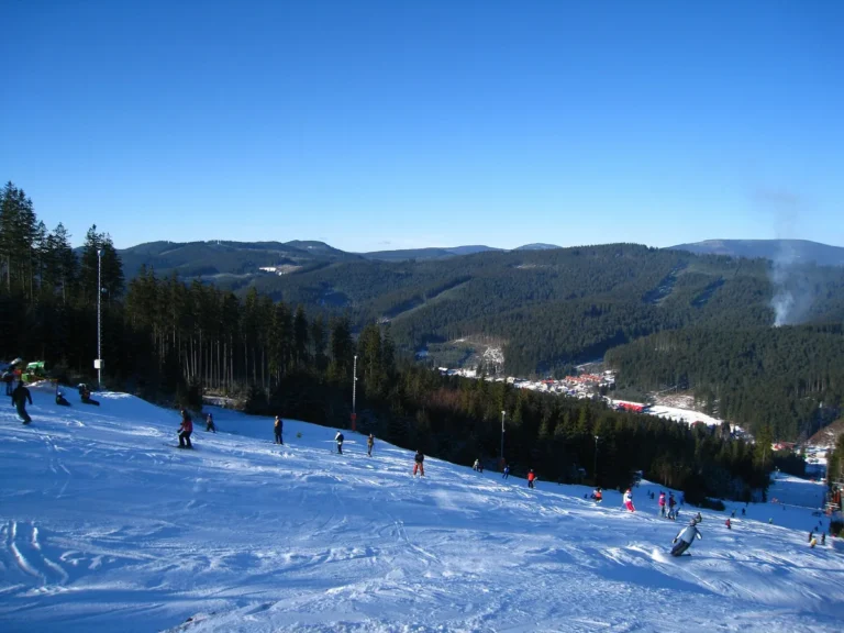 Pohled ze zasněžené sjezdovky ski areálu Bílá do údolí s obcí a na zalesněné hřebeny Beskyd