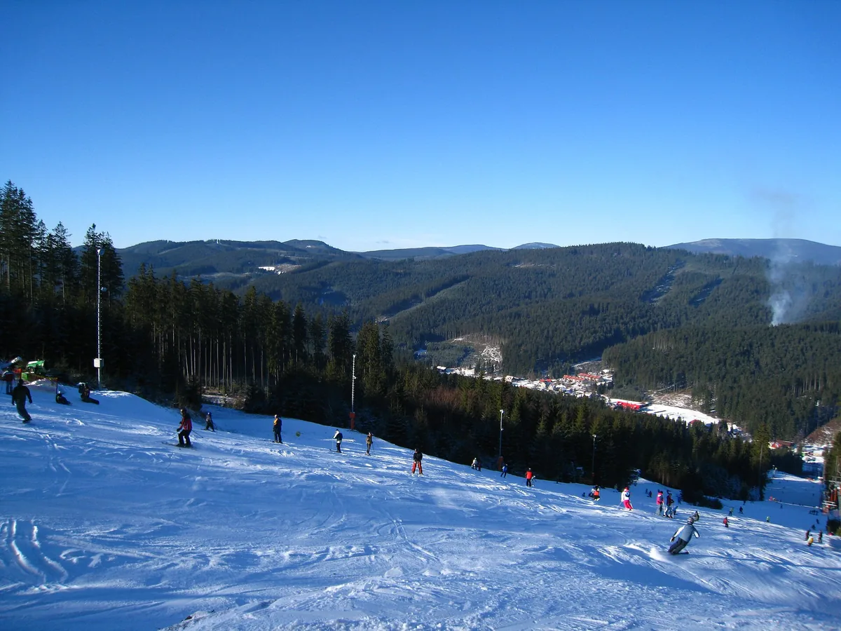 Pohled ze zasněžené sjezdovky ski areálu Bílá do údolí s obcí a na zalesněné hřebeny Beskyd
