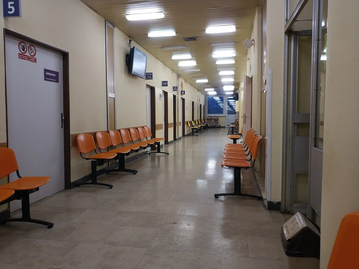 Prázdná chodba nemocničního pavilonu s řadami oranžových židlí pro čekající pacienty