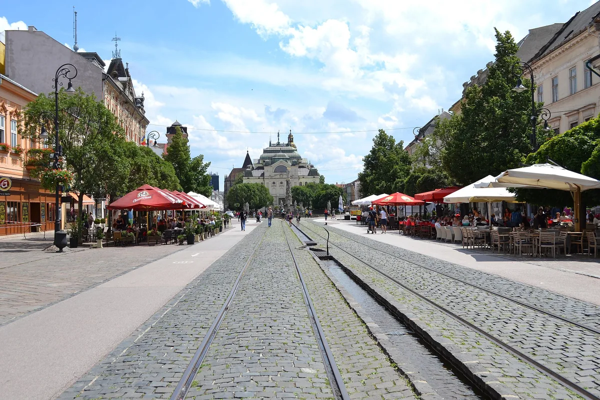 Pěší zóna na Hlavní ulici v Košicích s tramvajovými kolejemi, letními zahrádkami a budovou divadla v pozadí