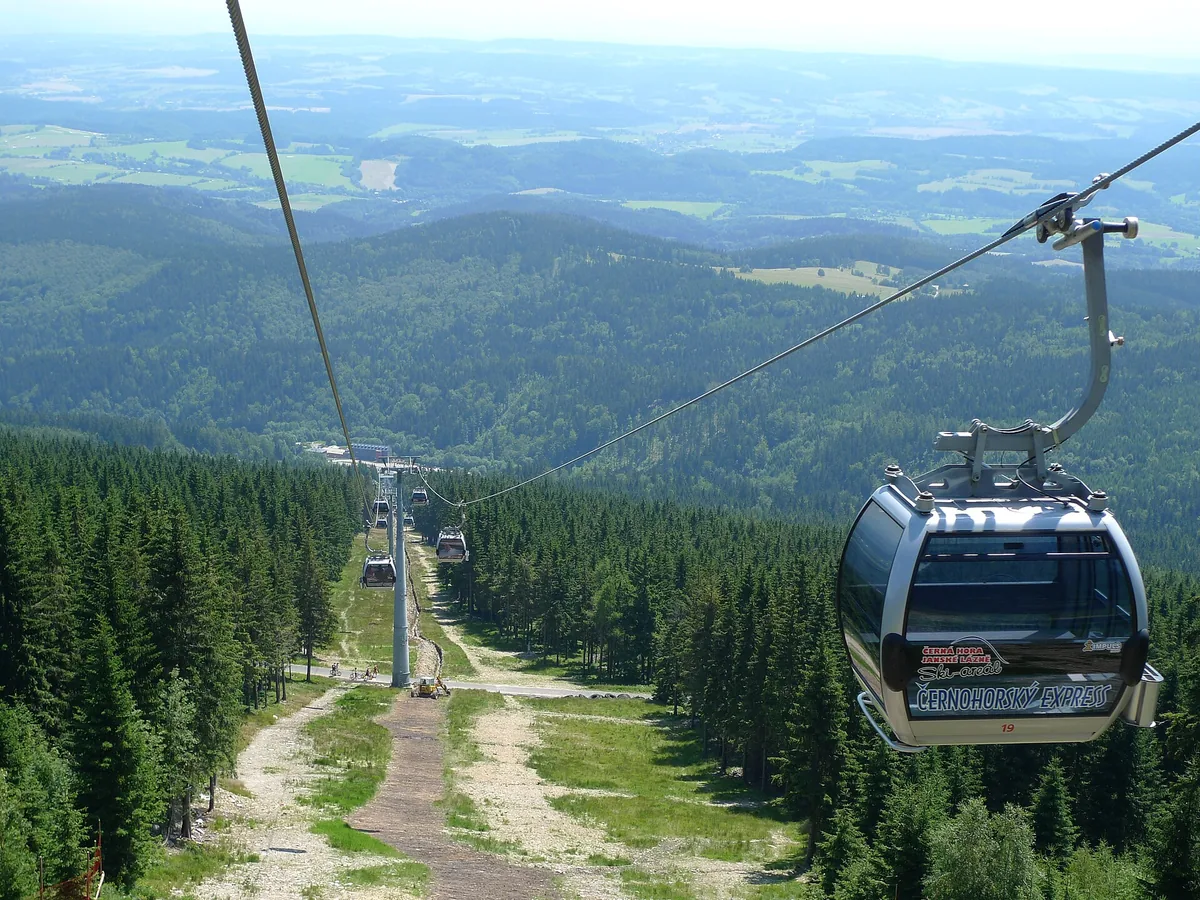 Kabinky lanovky Černohorský Express nad lesním průsekem při pohledu z kabinky dolů k Janským Lázním