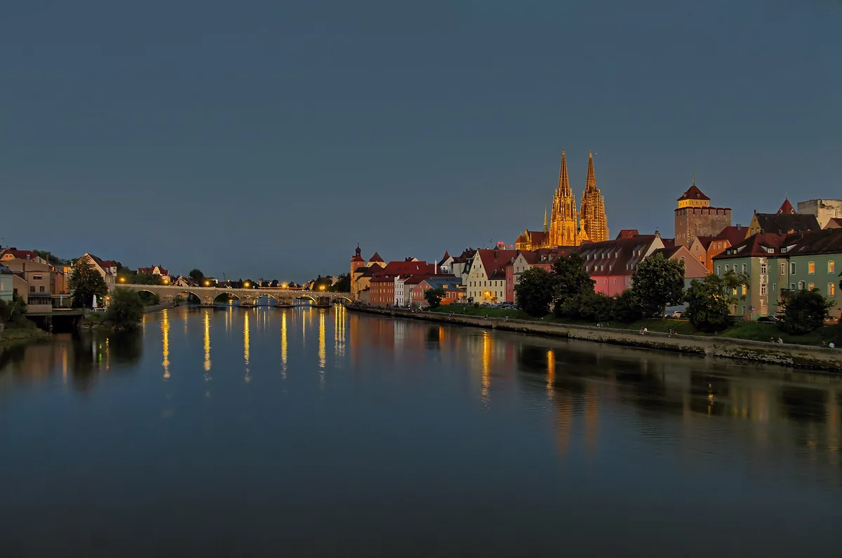 Večerní pohled přes Dunaj na Kamenný most a osvětlené věže dómu sv. Petra v Regensburgu