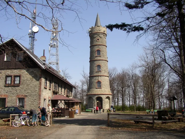 Kamenná rozhledna Jedlová se špičatou střechou a sousední restaurace na vrcholu hory v Lužických horách