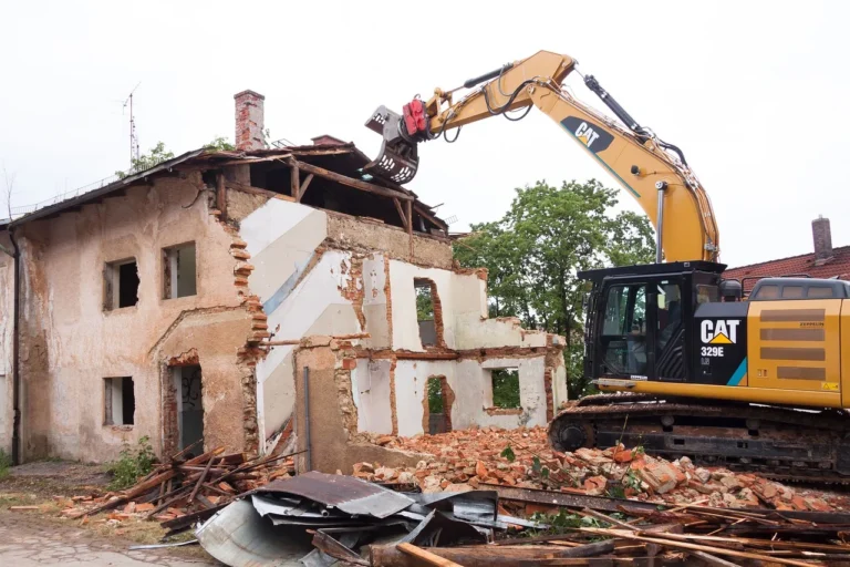 Bagr při demolici domu, před stavbou leží stavební suť.