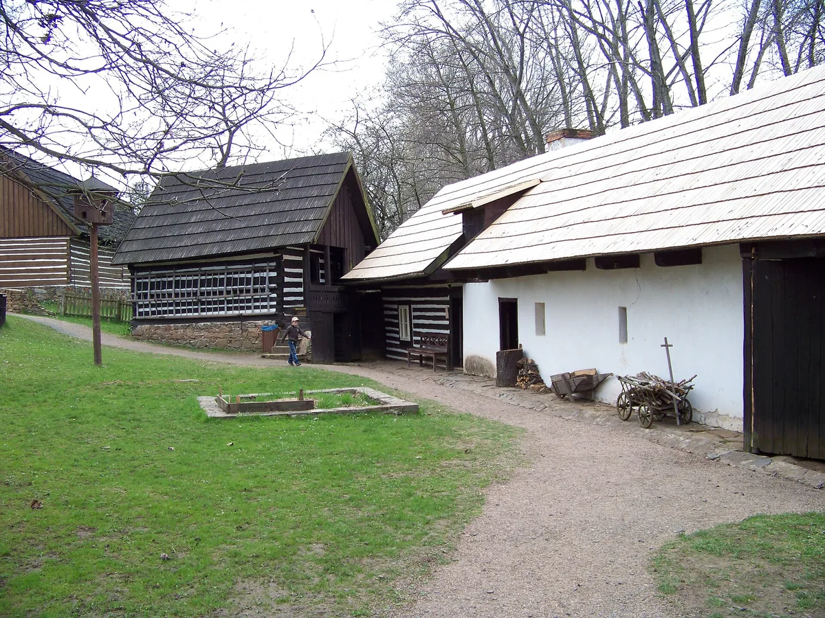 Roubená chalupa a špýchar z Budče vedle bíle omítnutého stavení v Muzeu lidových staveb v Kouřimi