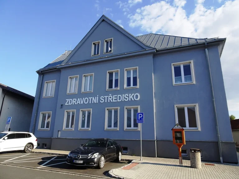 Modrá budova zdravotního střediska v Holýšově s nápisem na fasádě, snímek ze srpna 2022