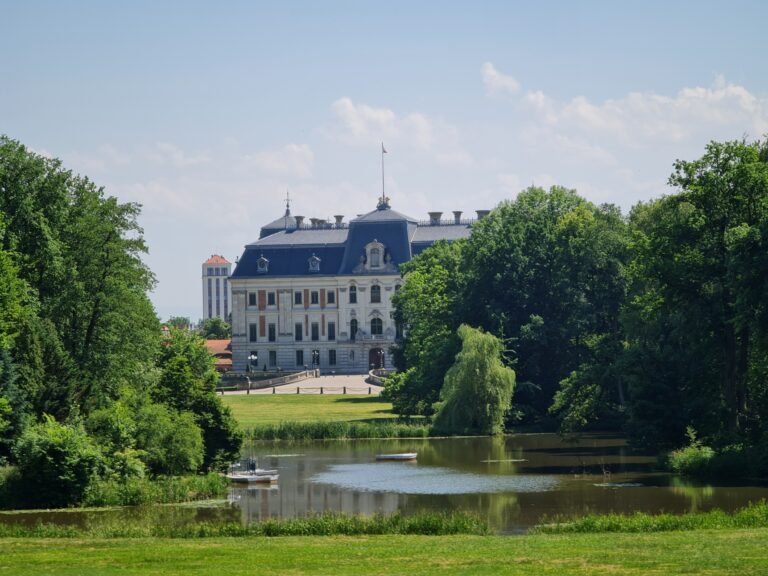 Světlá fasáda zámku Pszczyna za vodní plochou a zelení parku