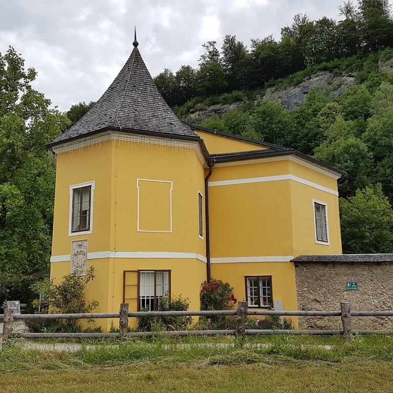 Žlutá vstupní budova Zoo Salzburg pod zalesněným svahem