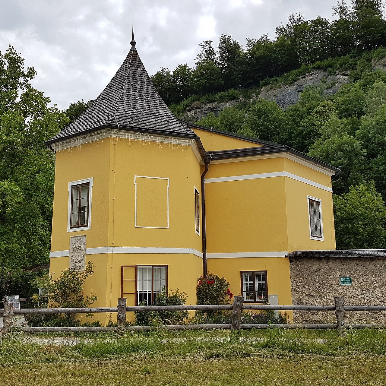 Žlutá vstupní budova Zoo Salzburg pod zalesněným svahem